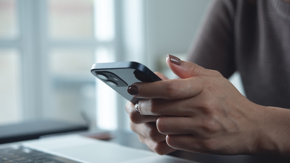 Mobile app development - Close-up of woman using smartphone while working on laptop at home office