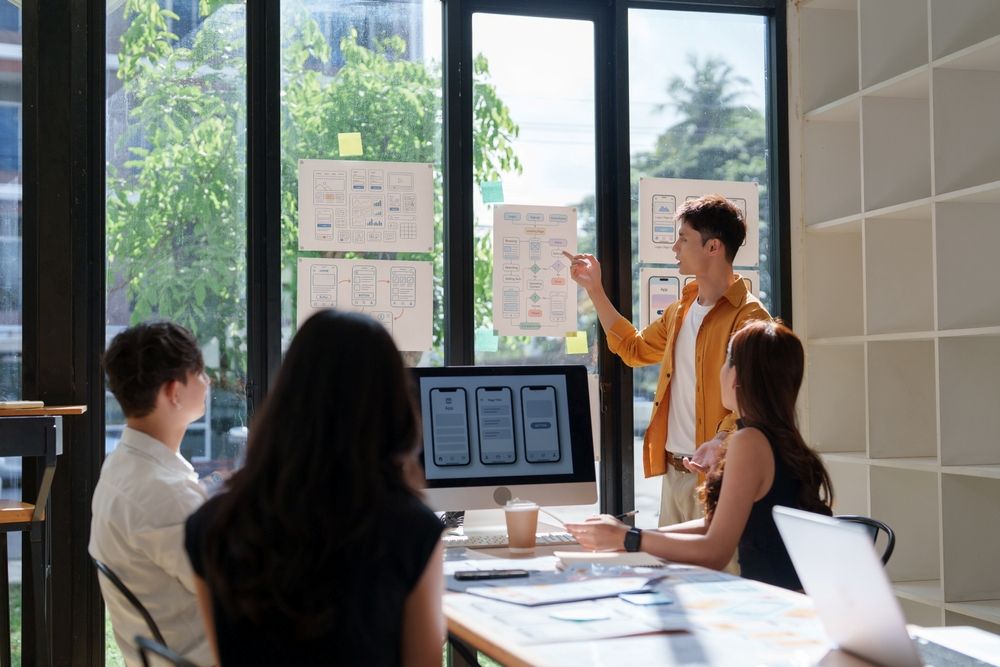 Mobile app development - Team of ux designers collaborating, developing user experience and mobile application interface wireframes in a modern office space with the sun beaming in