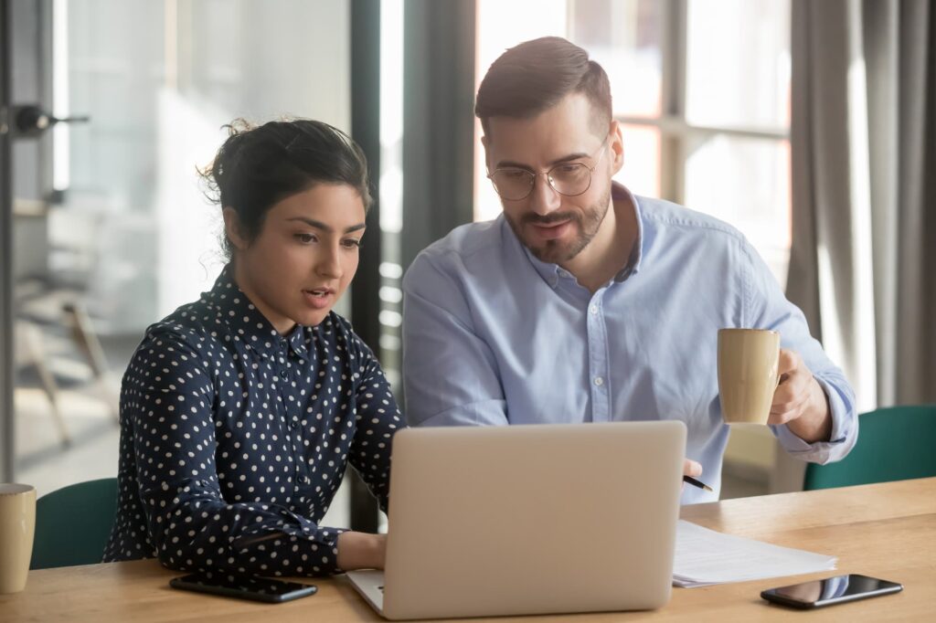 Data platforms and identity resolution - A man and a women sit at a table with a laptop, papers, and a smartphone; the man holds a coffee mug.


