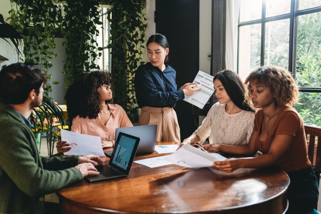 Sales forecasting - A group of people around a table, one standing and holding a document.
