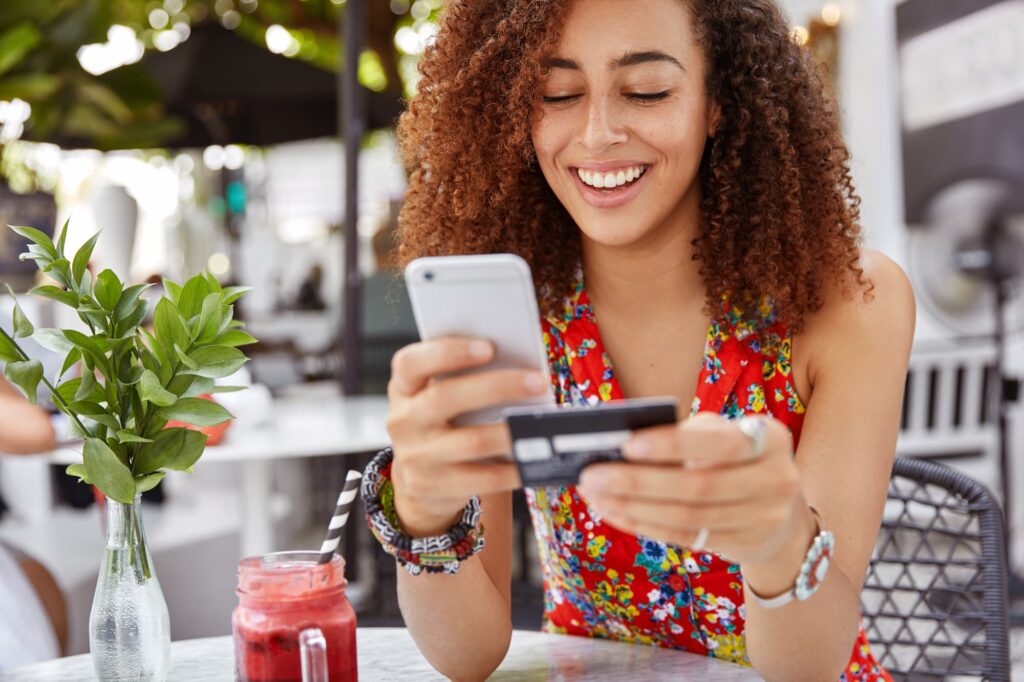 Customer experience consulting - Young women at an outdoor cafe holding a smartphone and credit card.

