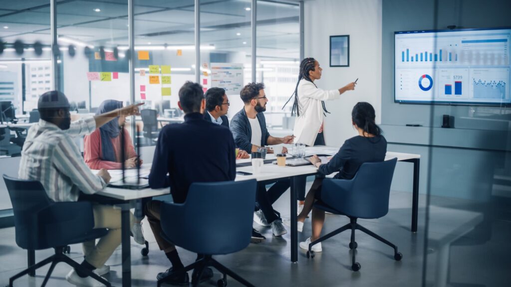 Data strategy - Group of people in a business meeting with one person presenting at a screen in a modern office.

