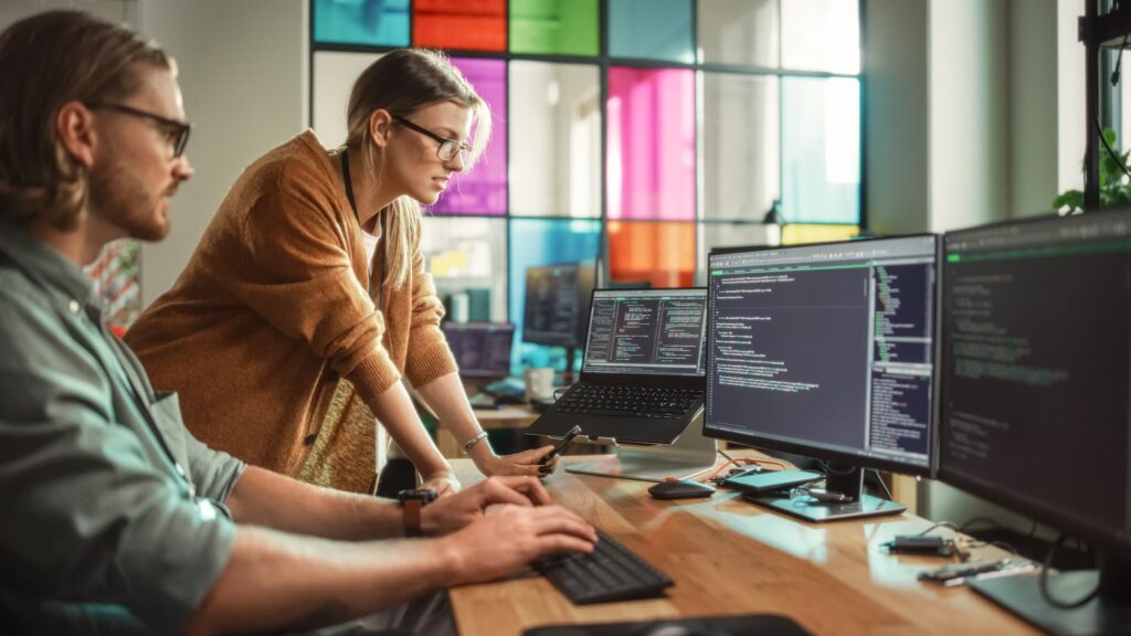 Data architecture - A man and women working at a desk with multiple monitors showing code. 


