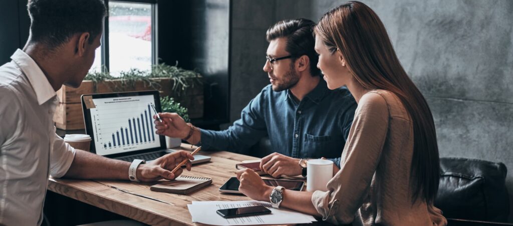 MarTech implementation - One women and two men sit at a table in an office, looking at a laptop screen. 
