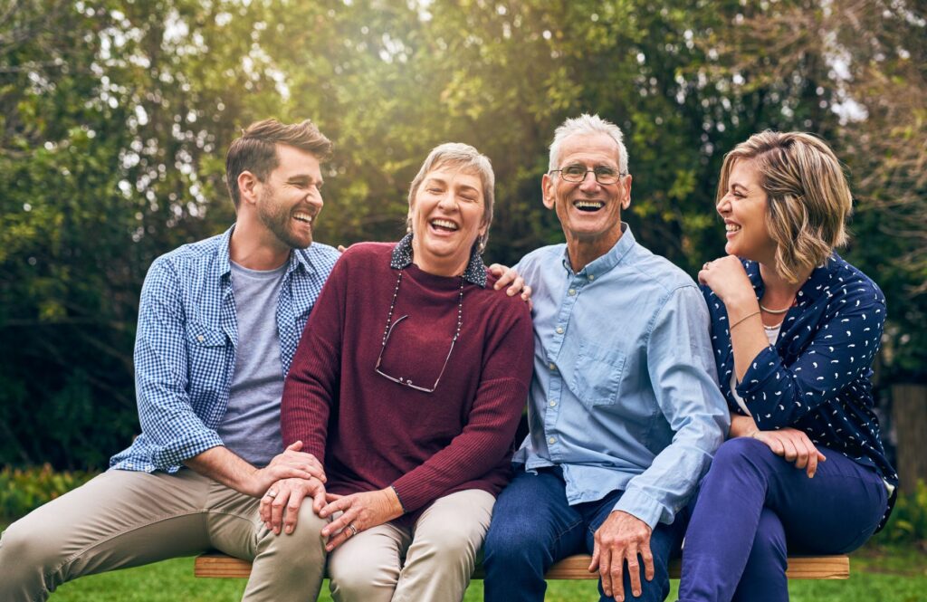 Family picture of grandchildren with grandparents sitting in between them, all of them are sitting on a bench.
