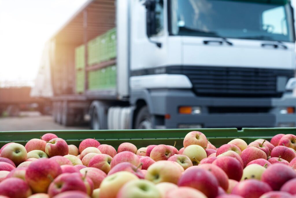 Crate full of apples with a food truck in the background with more crates being emptied