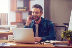 Gwynedd Council - Man calling on his phone while working on his laptop at home