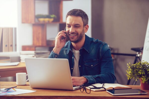 Gwynedd Council - Man calling on his phone while working on his laptop at home