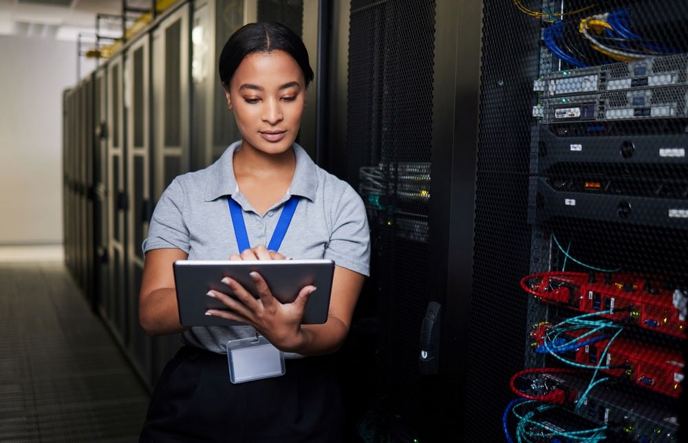 Woman using a tablet inside a server room during a routine inspection for cybersecurity