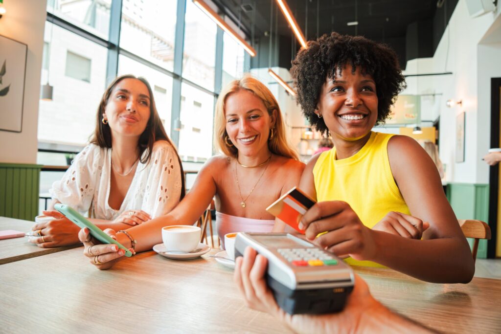A cheerful young woman is settling her bill with a contactless creditcard at a restaurant