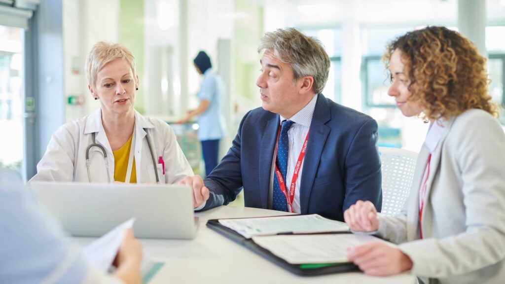 Three NHS workers in discussion over healthcare finances sitting around a round table