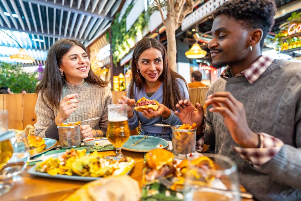 Group of happy multiethnic friends enjoying a meal together, eating burgers, fries and drinking beer
