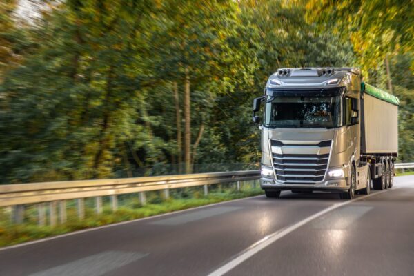Large modern truck on winding road through green forest.