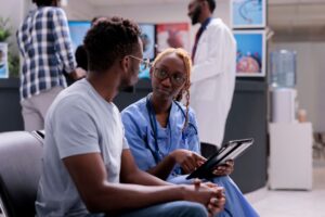 Female nurse and patient talking about disease, doing checkup consultation with sick man in hospital waiting area