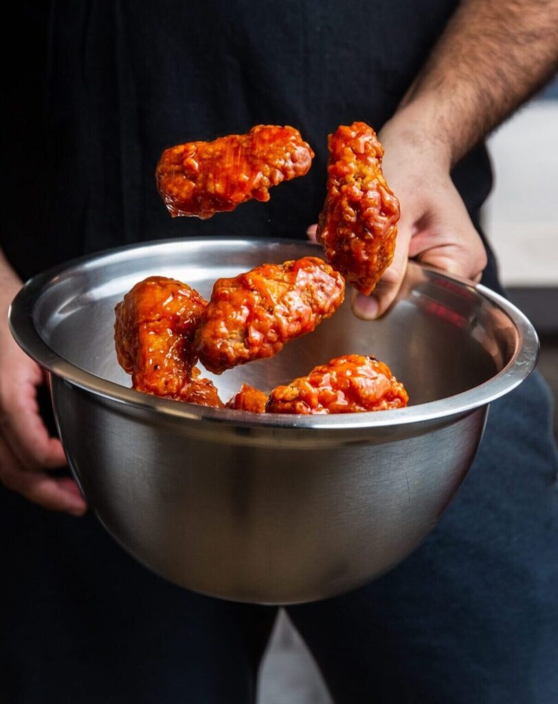 Saucy fried chicken wings coated with sauce tossed in the air
